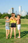 Three girls wearing Zilker Belts hugging in a park.