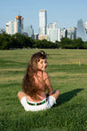 A girl is sitting in a field wearing Verde Kids from Zilker Belts.
