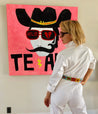 a woman in white standing next to a Zilker Belts ACL painting of a cowboy.