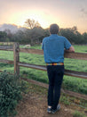 A man standing on a fence looking at a field of Zilker Belts cows.