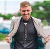 A man wearing a Zilker jacket and a Zilker Bolo Tie is smiling.