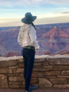 A woman wearing a Zilker Belts hat and jeans looking out over the grand canyon.