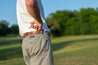 A man is standing on a Deep Eddy golf course wearing Zilker Belts.