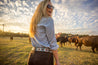 A woman in a Zilker Belts cowboy hat standing in front of a herd of cows.