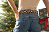 A woman is holding a Vagabond present from Zilker Belts in front of a Christmas tree decorated with Argentine leather ornaments.