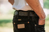 Close-up of a person wearing black jeans with a distinctive Zilker Belts Maverick Argentine leather black belt and a white t-shirt, viewed from the back.