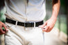 Close-up of a person in white pants fastening a black Zilker Belts Maverick Argentine leather belt.