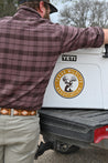 Man in a plaid shirt and khaki pants standing next to a white truck with "Zilker Belts" and "Texas Wildlife Association (PREORDER)" logos on it.