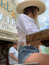 A woman wearing a Zilker Belts cowboy hat and shorts sitting at a table.
