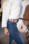 A woman is standing next to a horse wearing Zilker Belts' ATX Light jeans and a sweater.