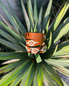 a pair of Zilker Belts Rambler orange leather bracelets sitting on top of a plant.
