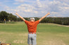 A man standing on a golf course with his arms outstretched, wearing Zilker Belts' ATX Kids.