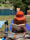 A woman laying on the grass reading a Zilker Belts ATX Rope Hat.