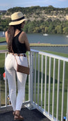 Girl wearing a light brown leather belt with black and white stitching. She styles it with white jeans, a black top, and a straw hat.