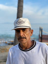 A man with a mustache standing near the ocean wearing a Zilker Belts Blanco Rope Hat.