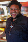 A man with dreadlocks smiling in front of a Zilker Belts bar wearing a Zilker Bolo Tie.