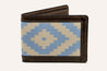 Introducing the Bouldin Creek Wallet by Zilker Belts, a meticulously handcrafted leather wallet showcasing a bi-fold design. It features geometric blue and beige Argentine woven fabric on the front, beautifully bordered and trimmed with rich dark brown leather.