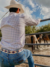 A man in a Zilker Belts cowboy hat is looking at horses from a fence.