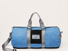 A Zilker x Old Enfield blue duffel bag with a black strap.