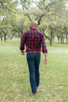 a man in a plaid shirt walking through a field wearing Zilker Belts' Landshark.