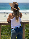 A woman wearing Zilker Belts jeans and a Zilker Belts hat looking at the ocean.