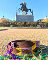Zilker Belts Mardi Gras beads on the ground in front of a statue.