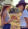Two women in cowboy hats holding cans of Zilker Belts Native beer.