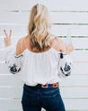 A woman wearing a white Waterloo top and jeans holding a peace sign.