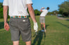 A man is holding a Save Muny golf club while another man is holding a Zilker Belts golf club.