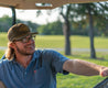 a man wearing a Greenbelt Rope Hat from Zilker Belts driving a golf cart.